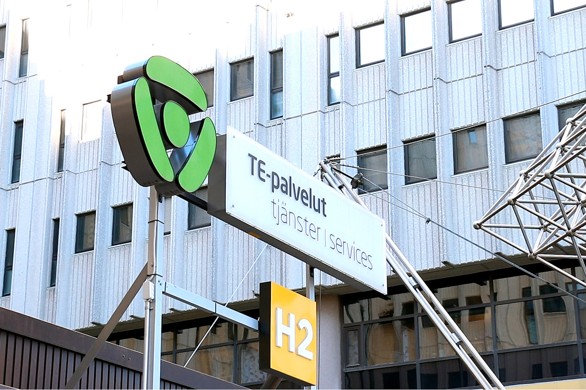 Valokuvassa TE-palveluiden kyltti, taustalla harmaa toimistorakennus.