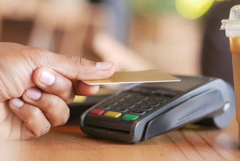 Käsi pitelee maksukorttia maksulaitteen yläpuolella.