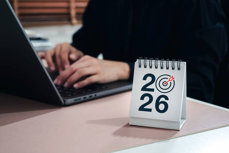 A person at a computer. On the table is a calendar with the number 2026.