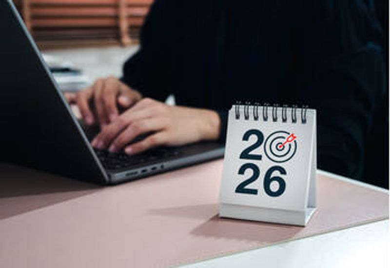 A person at a computer. On the table is a calendar with the number 2026.