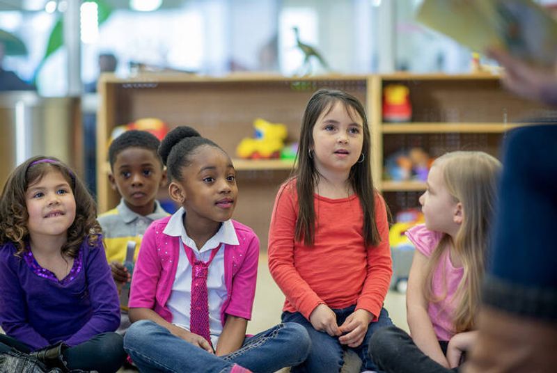 Valokuvassa lapsia istumassa lattialla, taustalla näkyy hyllyissä leluja.