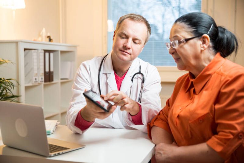 Valokuvassa lääkäri ja potilas, lääkäri esittelee testituloksia tablettitietokoneen näytöltä.