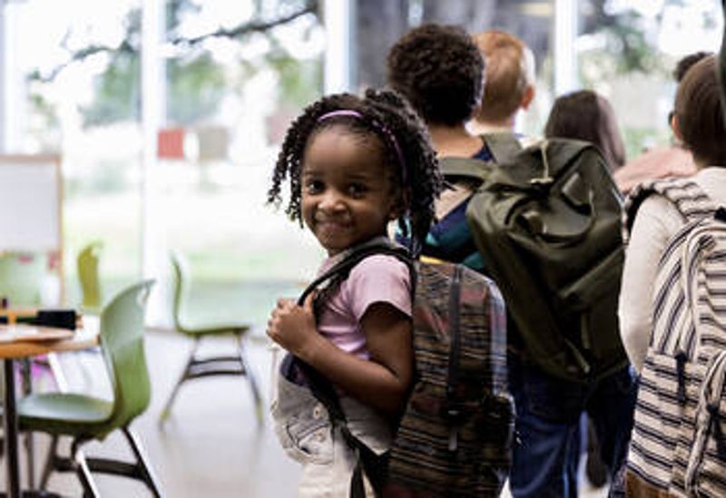 Kuvassa hymyilee maahanmuuttajataustainen tyttö koulussa. 