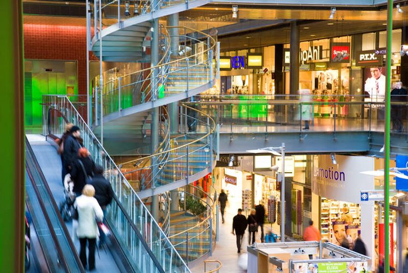 Ostoskeskus, jossa ihmisiä käytävällä ja liukuportaissa. 