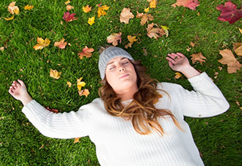 Nuori nainen makaa silmät kiinni nurmikolla, jossa on syksyn lehtiä.