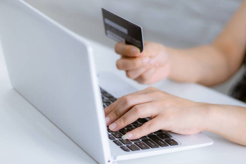 Käsi kannettavan tietokoneen näppäimistöllä, toinen käsi pitelee luottokorttia.